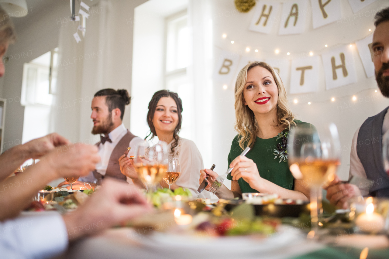 A happy big family sitting at a table on a indoor birthday party, eating.