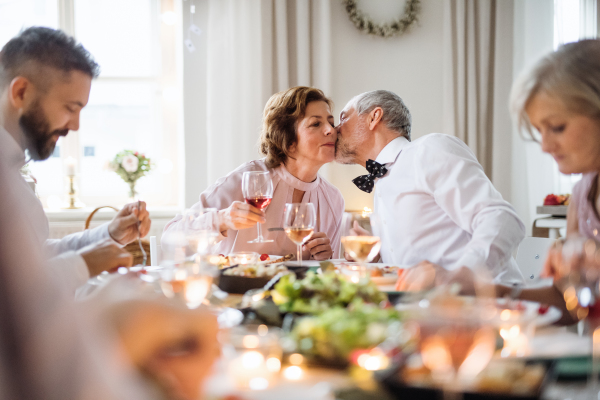 A senior couple sitting at a table on a indoor birthday party, kissing when eating.