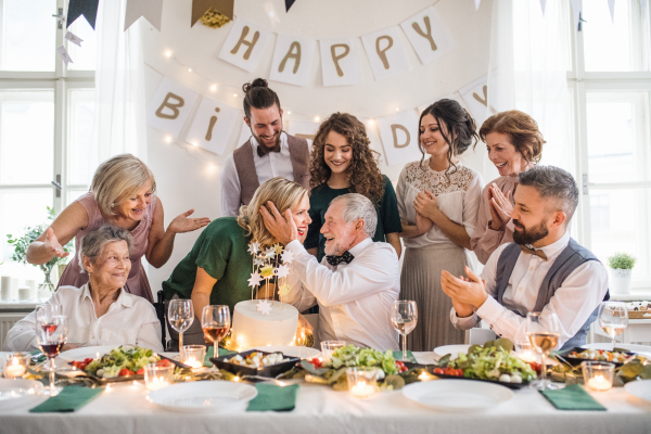 A senior man with multigeneration family and a cake celebrating birthday on an indoor party.