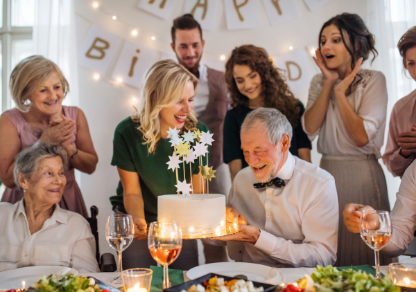 A senior man with multigeneration family and a cake celebrating birthday on an indoor party.