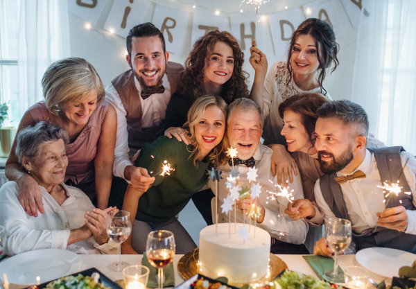 A senior man with multigeneration family and a cake celebrating birthday on an indoor party.