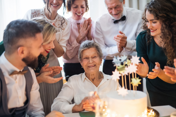 An elderly woman with multigeneration family and a cake celebrating birthday on an indoor party.