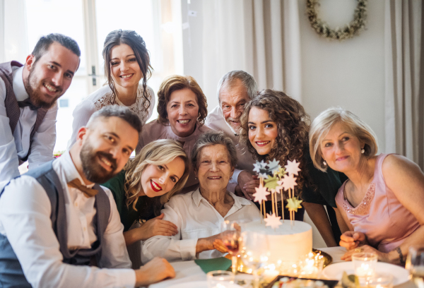 An elderly woman with multigeneration family and a cake celebrating birthday on an indoor party.