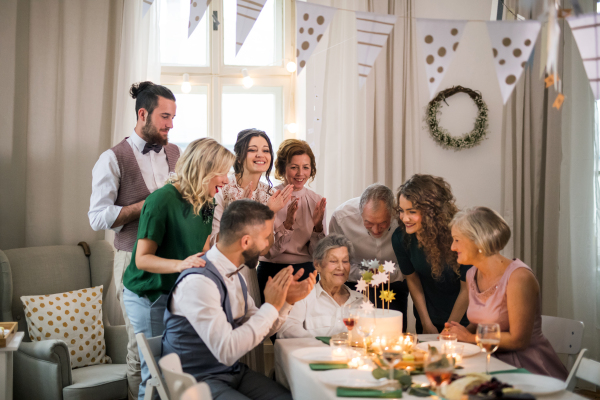 An elderly woman with multigeneration family and a cake celebrating birthday on an indoor party.