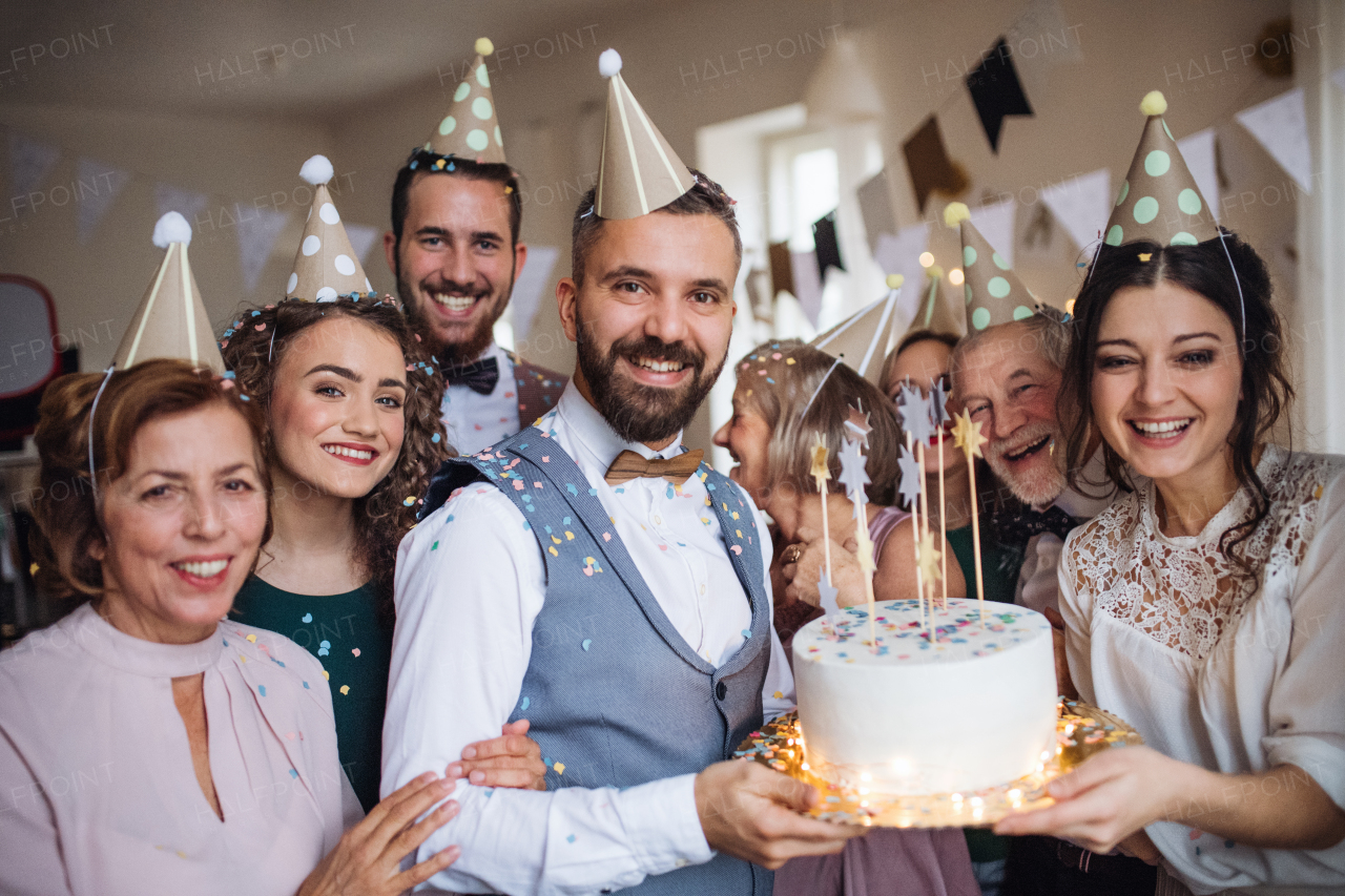 A portrait of multigeneration family with a cake and party hats on a indoor birthday party.