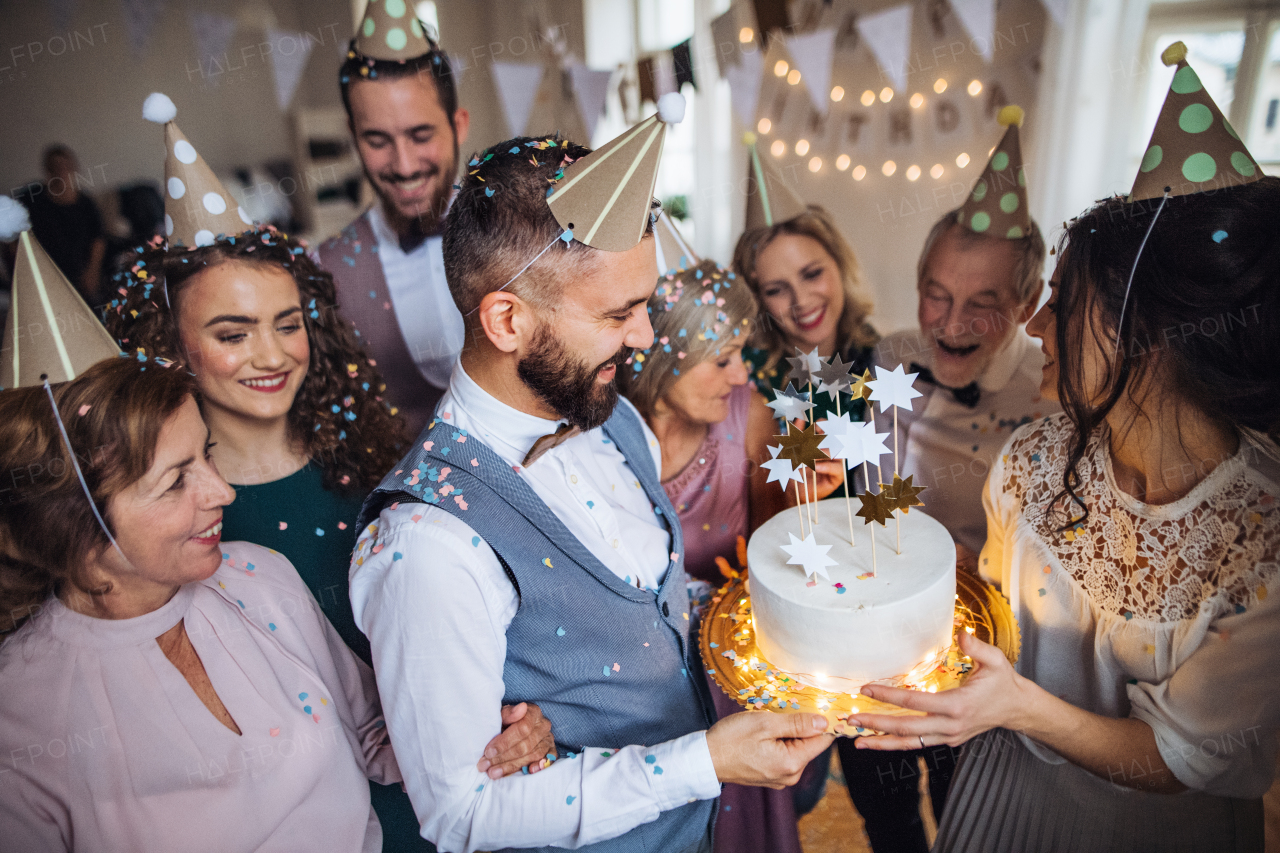 A portrait of multigeneration family with a cake and party hats on a indoor birthday party.