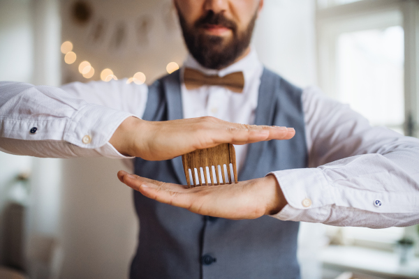 A midsection of man standing indoors in a room set for a party, holding a beard comb.