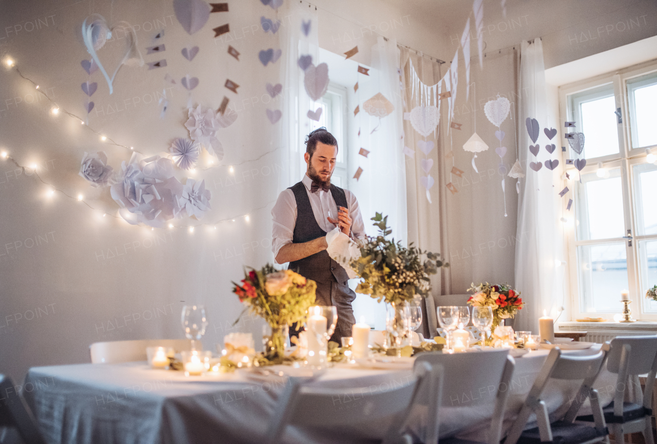 A young man with bow and vest setting a table for an indoor party.