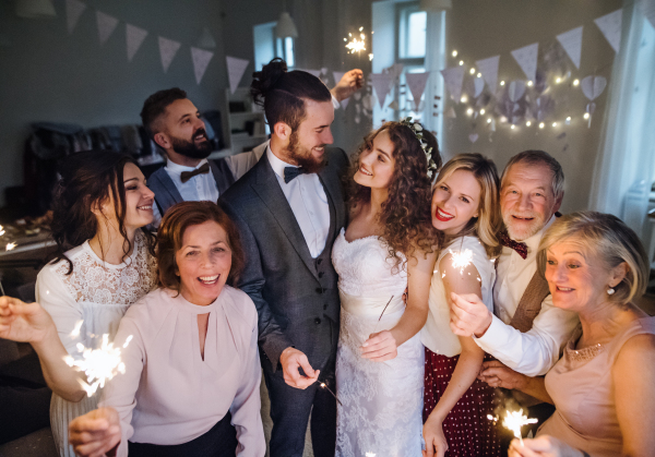 A young bride, groom and other guests posing for a photograph on a wedding reception, holding sparkles.