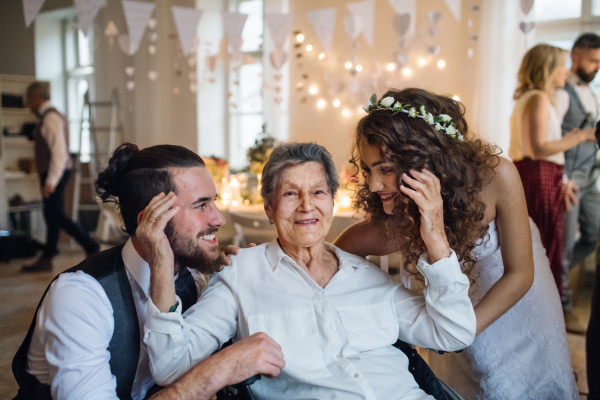 A young couple of bride and groom with grandmother on a wedding reception, posing for a photograph.