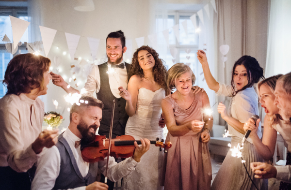 A young cheerful bride, groom and other guests dancing, singing and playing violin on a wedding reception.