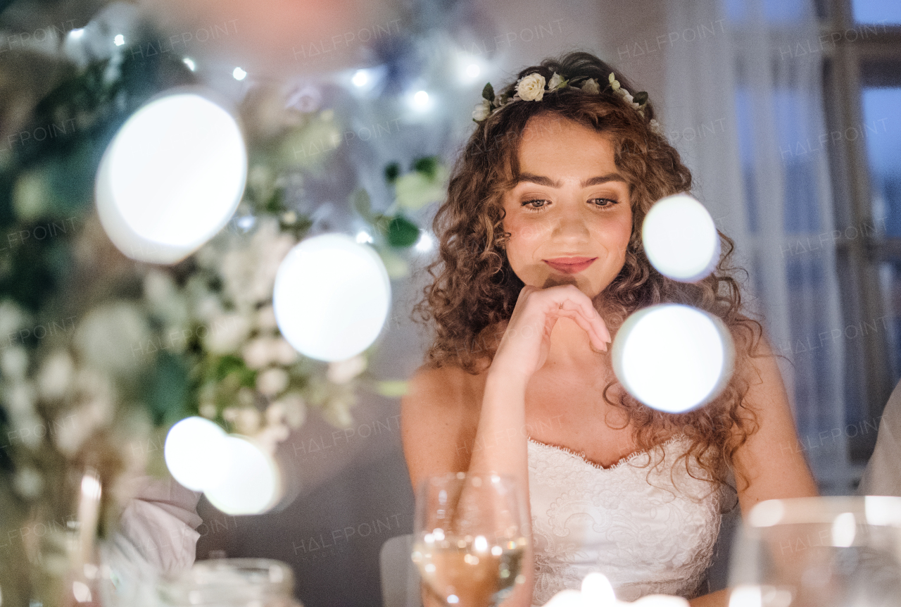 A front view of a thoughtful young bride sitting at a table on a wedding. Copy space.