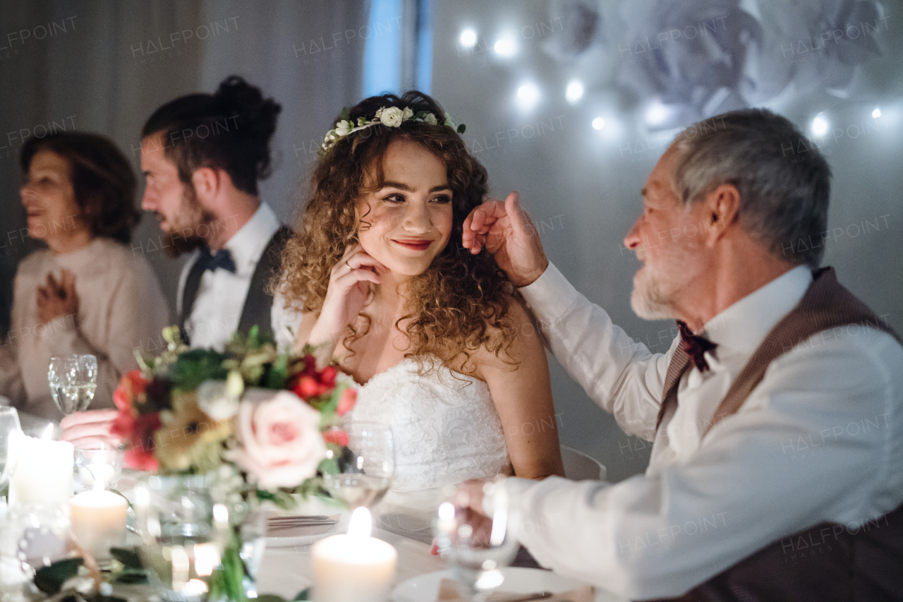 A loving father and beautiful bride sitting at the table on a wedding, talking and stroking her.