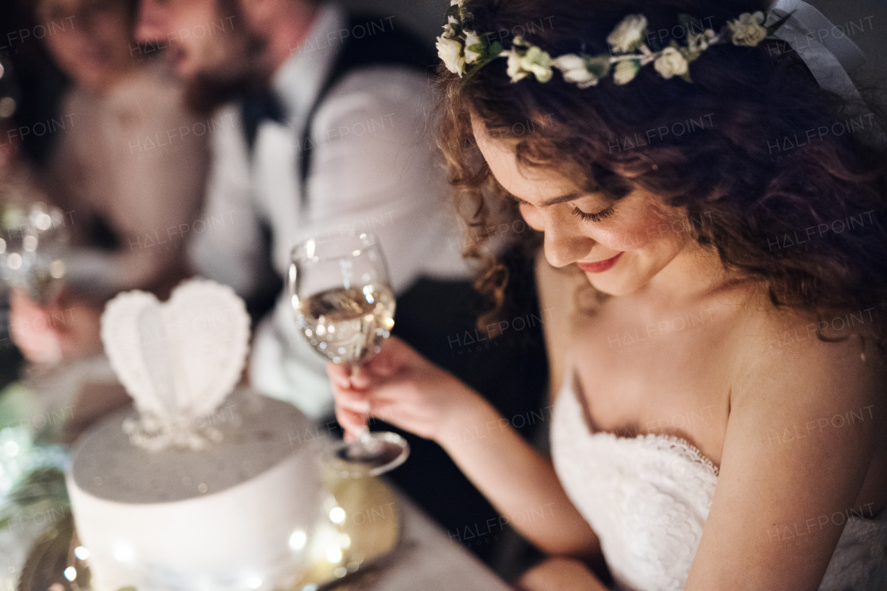 A close-up of a young bride sitting at a table on a wedding, holding a glass of white wine.