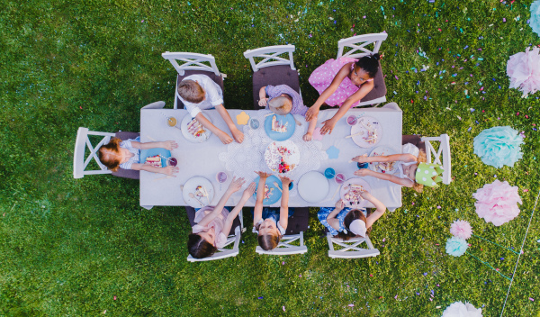 Top view of small children sitting at the table outdoors on garden party, eating cake.