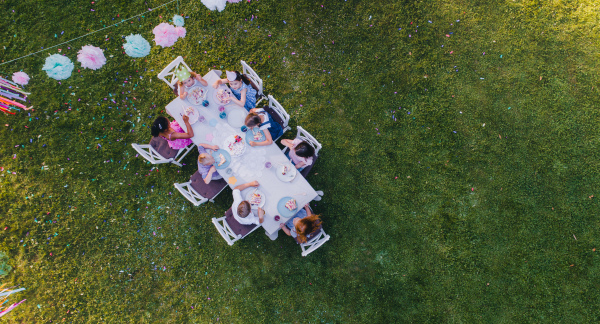 Aerial view of small children sitting at the table outdoors on garden party in summer, eating.