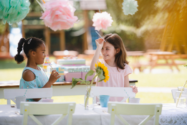 Small girls talking outdoors in garden in summer, a birthday celebration concept.