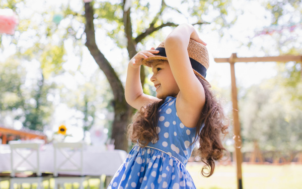 Small girl standing outdoors in garden in summer, a birthday celebration concept.