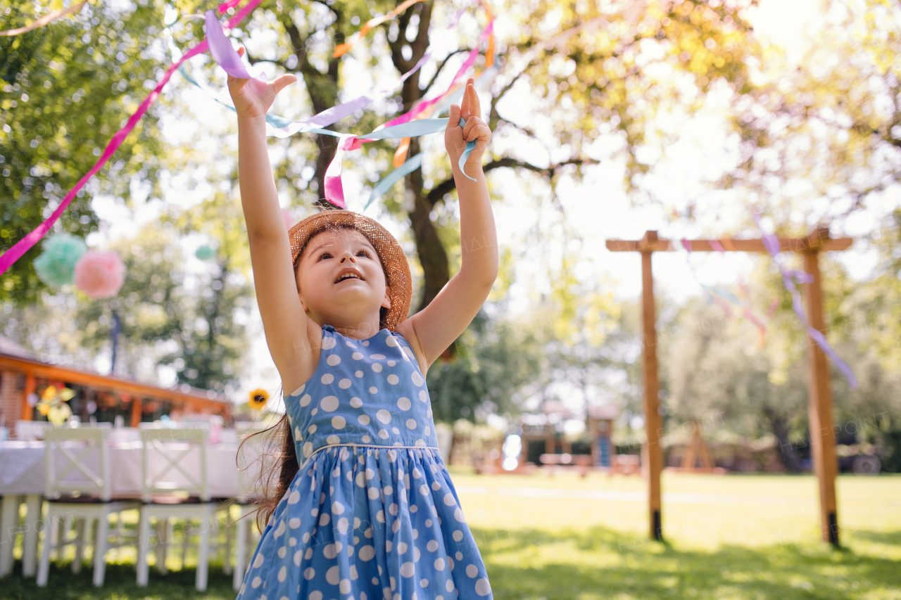 Small girl standing outdoors in garden in summer, a birthday celebration concept.