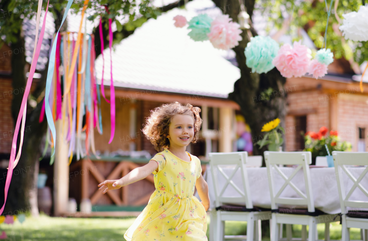 Small girl running outdoors in garden in summer, a birthday celebration concept.