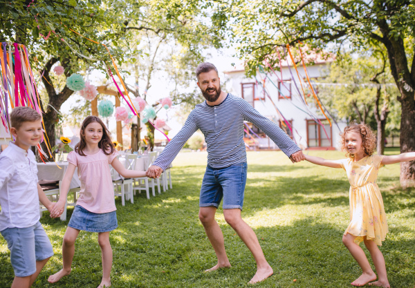 Man with group of kids on birthday party playing outdoors in garden in summer, celebration concept.