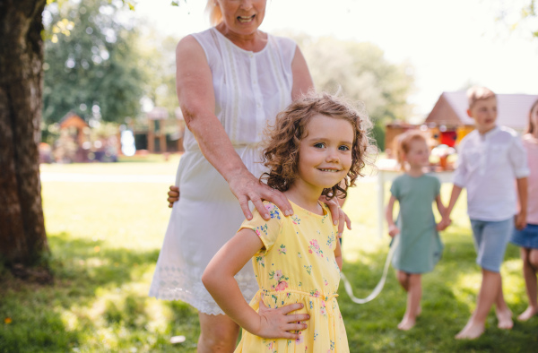 Small children with grandmother outdoors in garden in summer, playing.