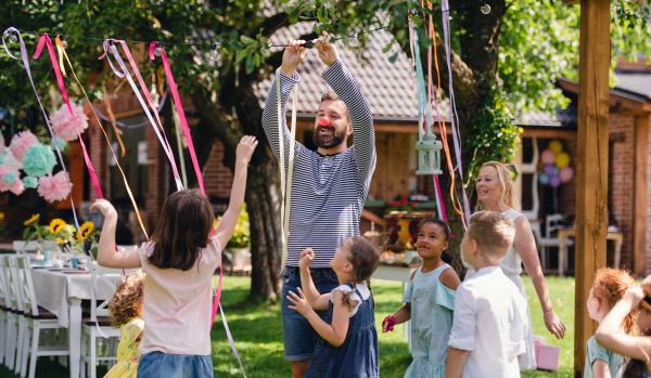 Man with group of kids on birthday party playing outdoors in garden in summer, celebration concept.