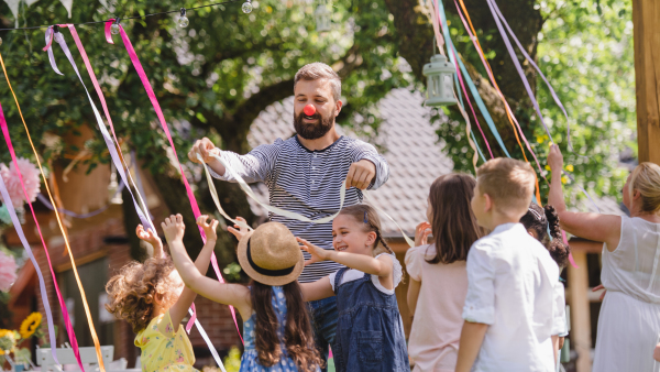 Man with group of kids on birthday party playing outdoors in garden in summer, celebration concept.