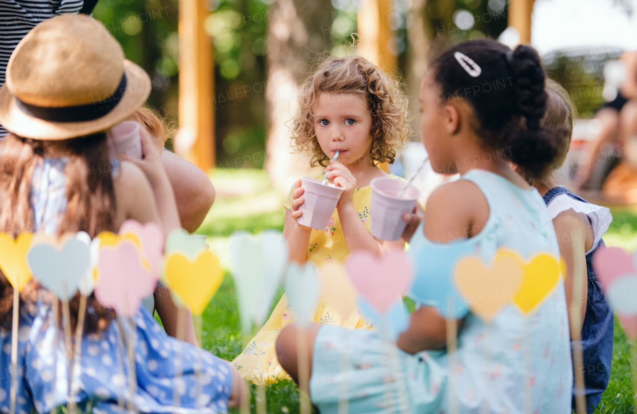 Small children sitting on ground outdoors in garden in summer, drinking. A celebration concept.