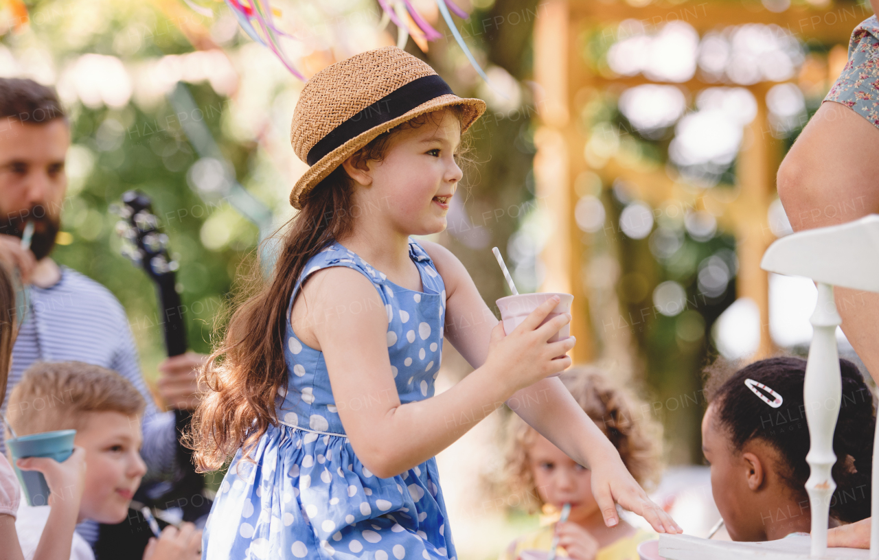 Small children on ground outdoors in garden in summer, playing and drinking.