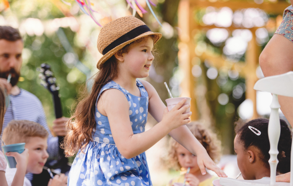 Small children on ground outdoors in garden in summer, playing and drinking.