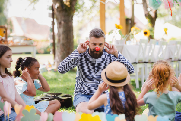 A man with small children sitting on ground outdoors in garden in summer, playing.