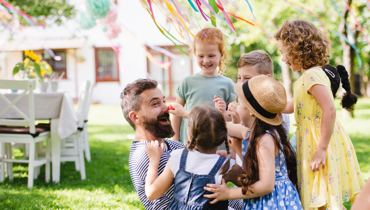 A man with small children sitting on ground outdoors in garden in summer, playing.