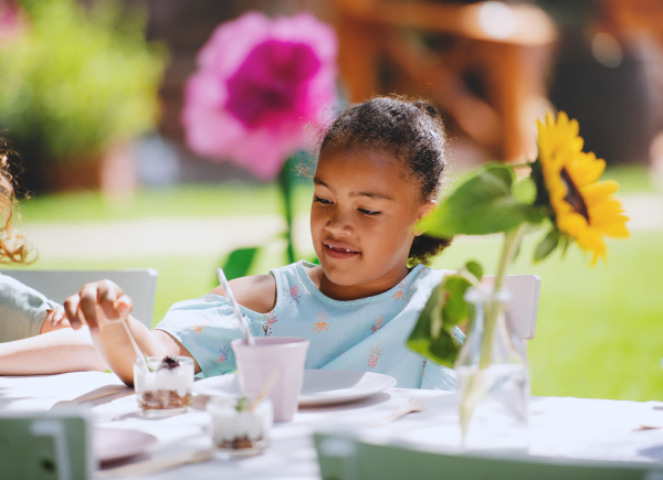 Small girl sitting outdoors in garden in summer, eating snacks. A celebration concept.