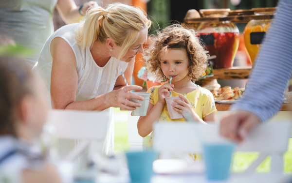 A grandmother and small girl outdoors on garden party in summer, drinking.