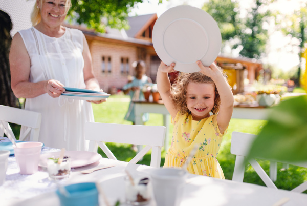 Grandmother and small girll outdoors on garden party in summer, setting table. A celebration concept.