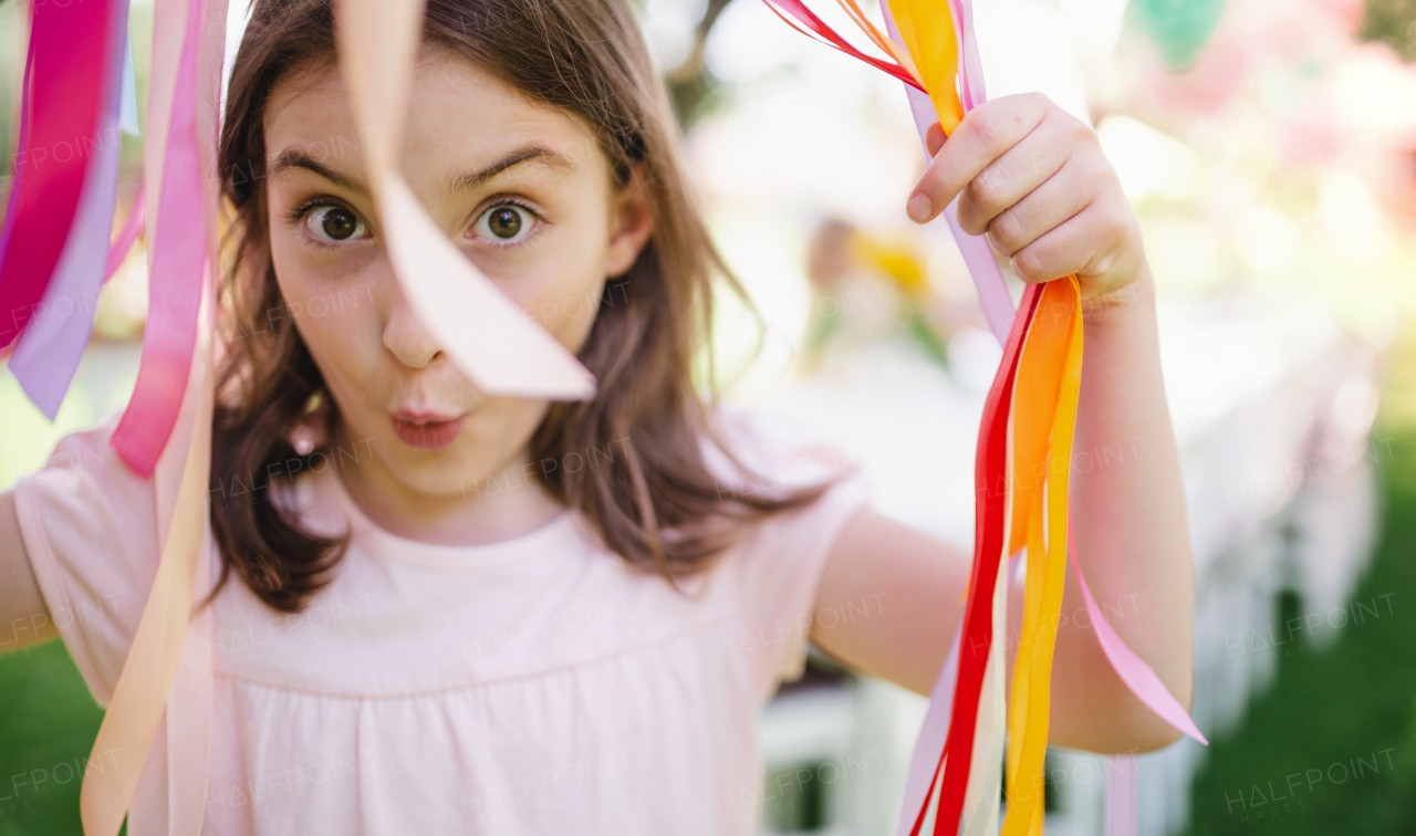 Small girl standing outdoors in garden in summer, a birthday celebration concept.