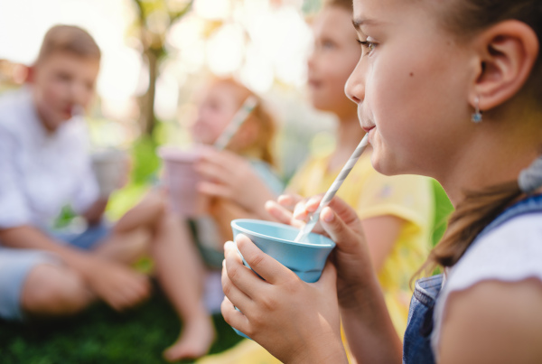 Small children sitting on ground outdoors in garden in summer, drinking. A celebration concept.