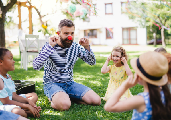 A man with small children sitting on ground outdoors in garden in summer, playing.