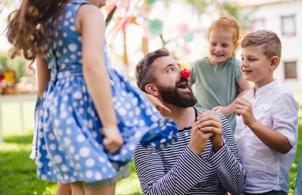 A man with small children sitting on ground outdoors in garden in summer, playing.