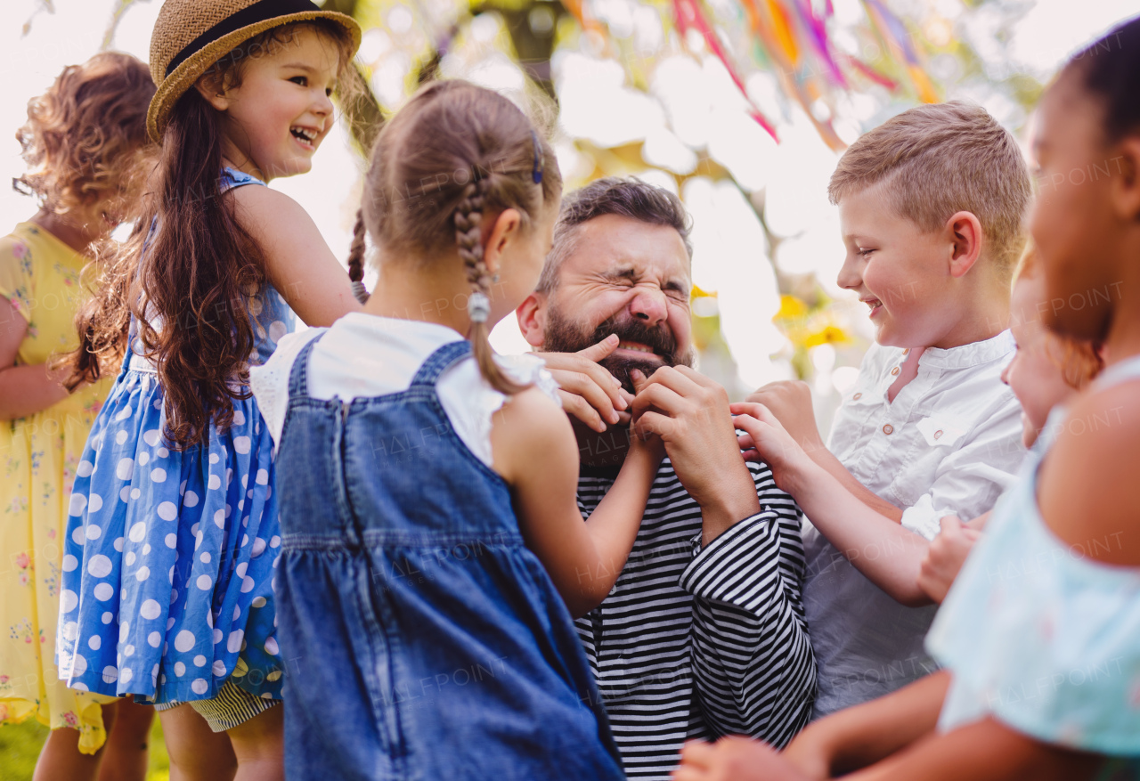 A man with small children sitting on ground outdoors in garden in summer, playing.