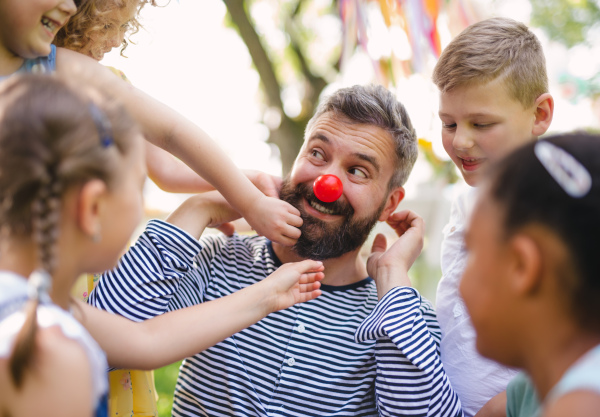 A man with small children sitting on ground outdoors in garden in summer, playing.