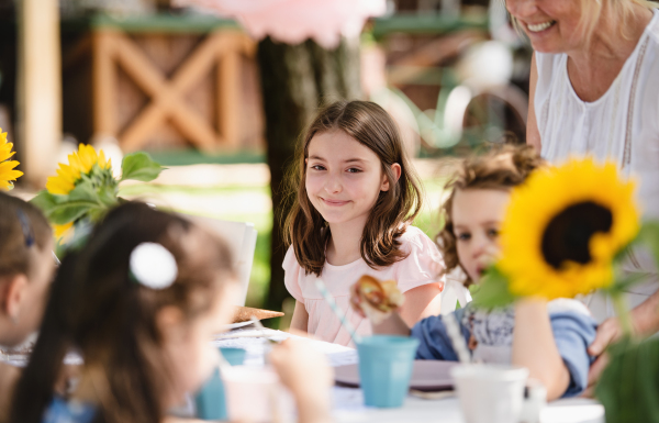 Happy small girls sitting and eating at table on summer garden party, birthday celebration concept.