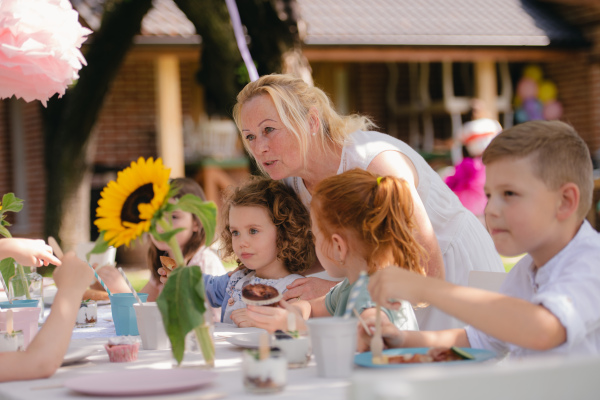 Group of small children sitting at the table outdoors on garden party, eating.