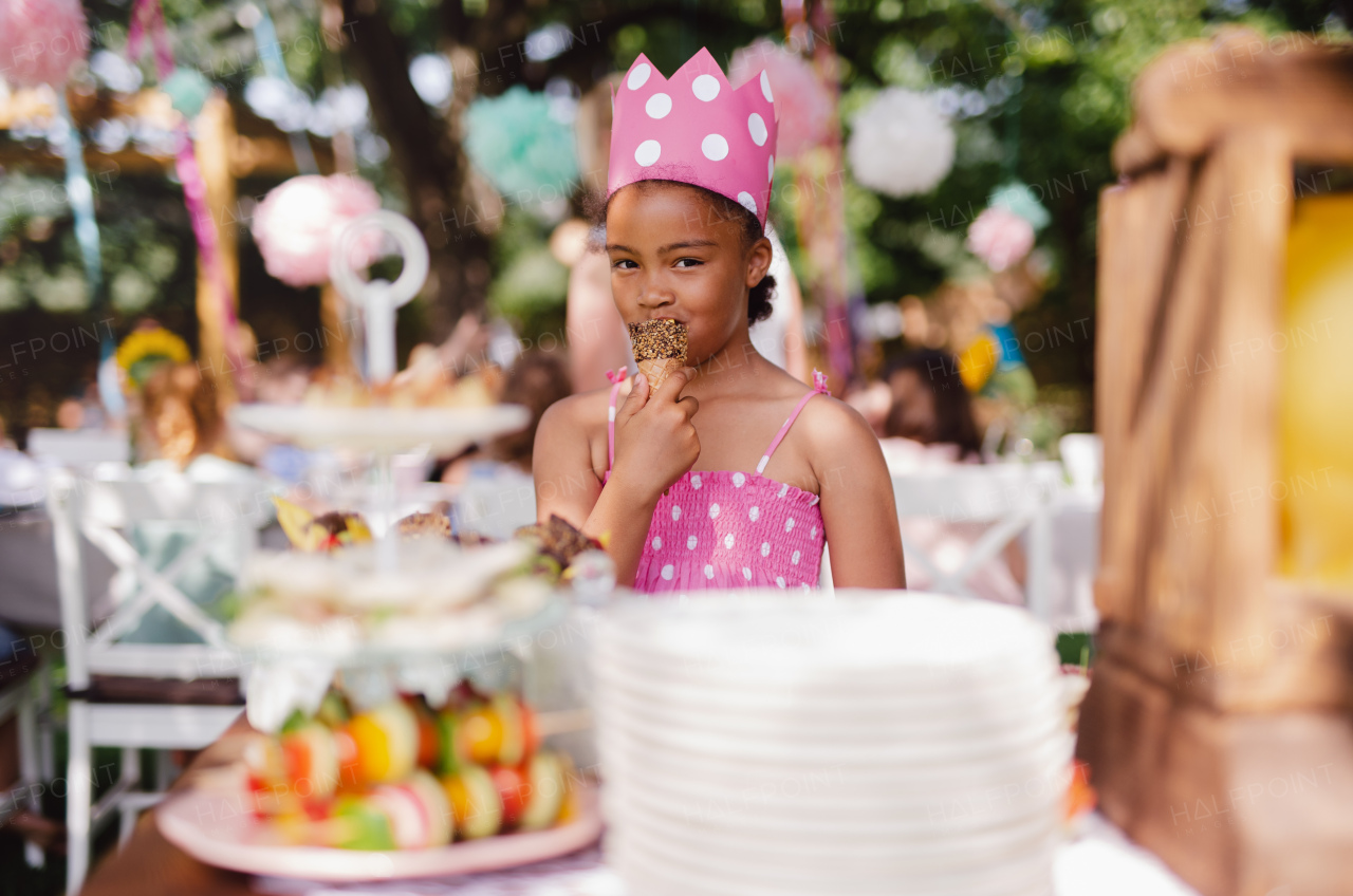 Small girl standing outdoors in garden in summer, a birthday celebration concept.