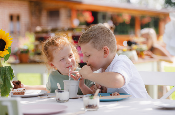 Group of small children sitting at the table outdoors on garden party, eating and drinking.