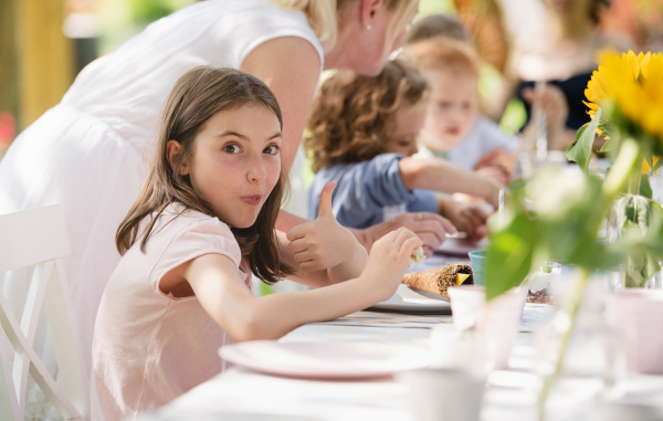 Group of small children sitting at the table outdoors on garden party in summer, eating.