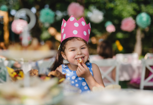 Cheeky small girl outdoors in garden in summer, eating snacks. A celebration concept.