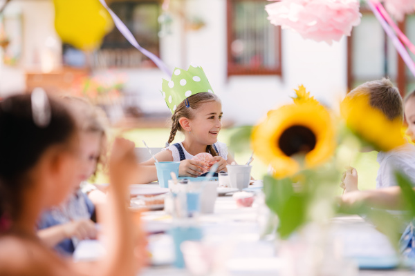 Group of small children sitting at the table outdoors on garden party in summer, eating.