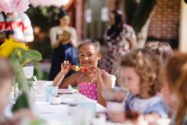 Group of small children sitting at the table outdoors on garden party, eating.